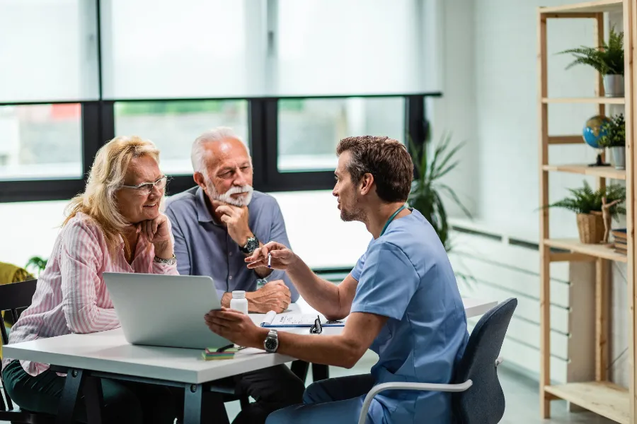 Physician reviewing information on a laptop with an older couple at a practice desk